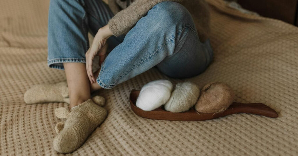 woman-sitting-on-a-bed-with-yarn-rolls-wearing-cozy-slippers-creating-a-warm-knitting-ambiance